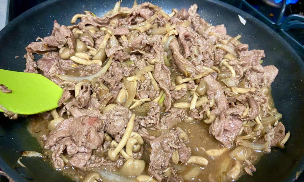 beef, onions, and mushrooms cooking in a pan